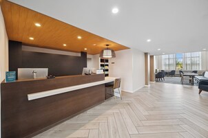 Un área de recepción con un mostrador de madera, una lámpara colgante y un espacio de espera con sillas y una mesa.