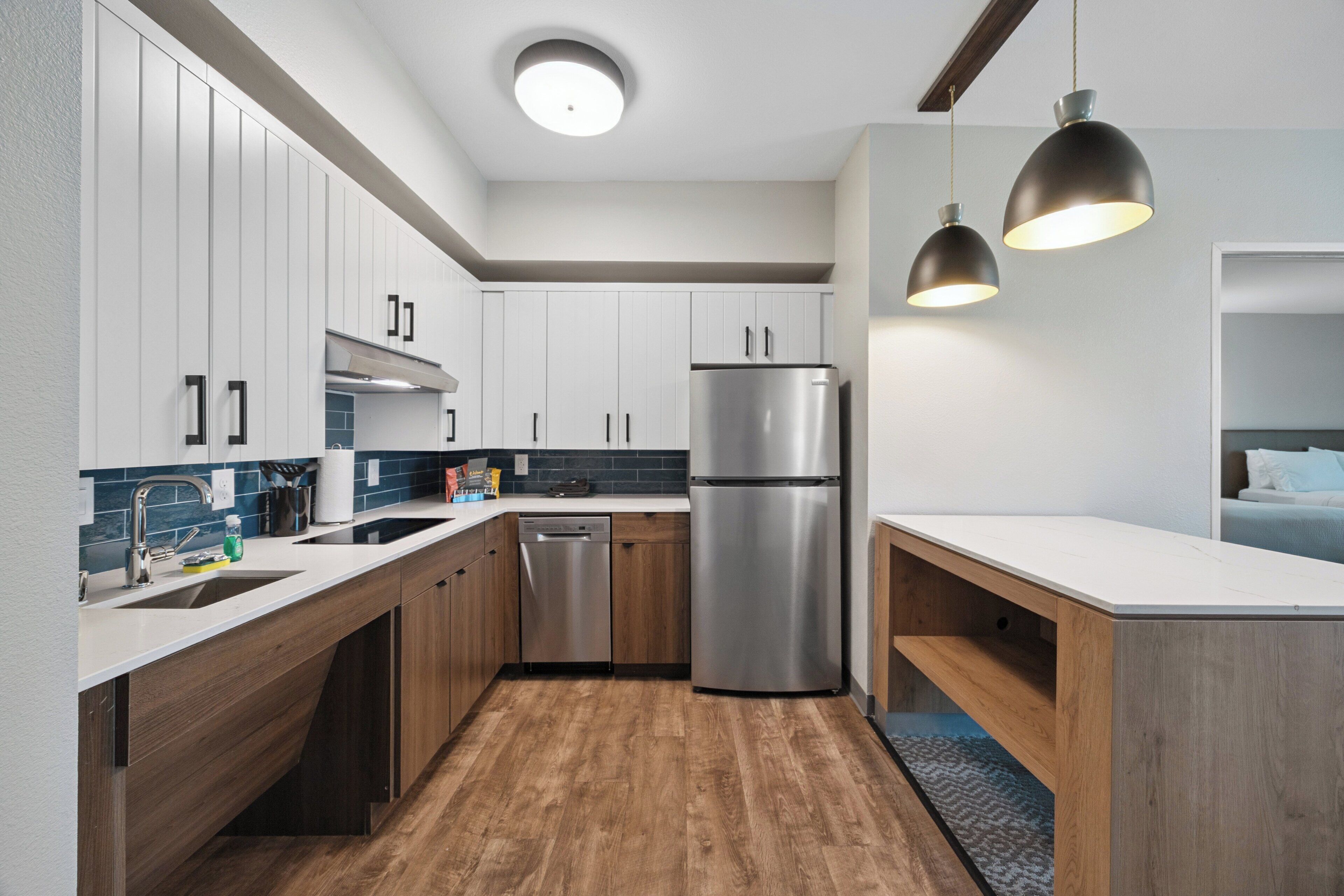 A modern kitchen with white cabinets, a stainless steel refrigerator, and pendant lighting.