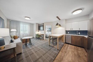 Una habitación de hotel moderna con sala de estar, una mesa de comedor, una cocina con armarios de madera y un escritorio integrado.