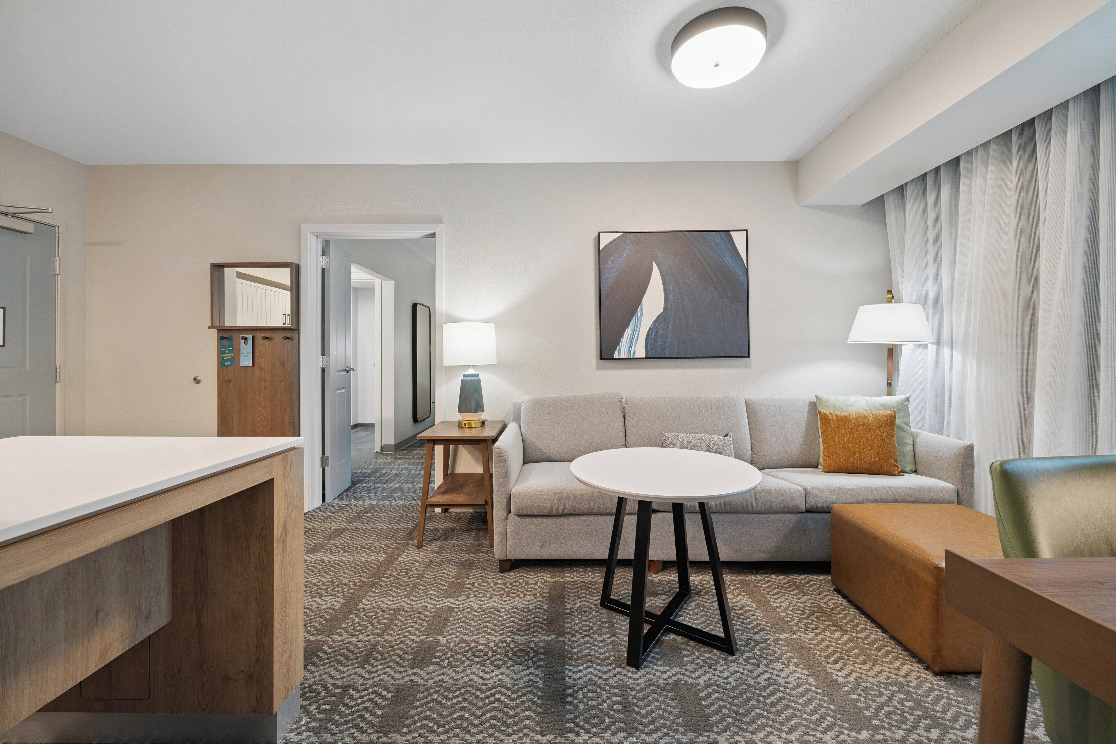 Een hotelkamer met een bank, een ronde tafel, een houten bureau en een lamp.