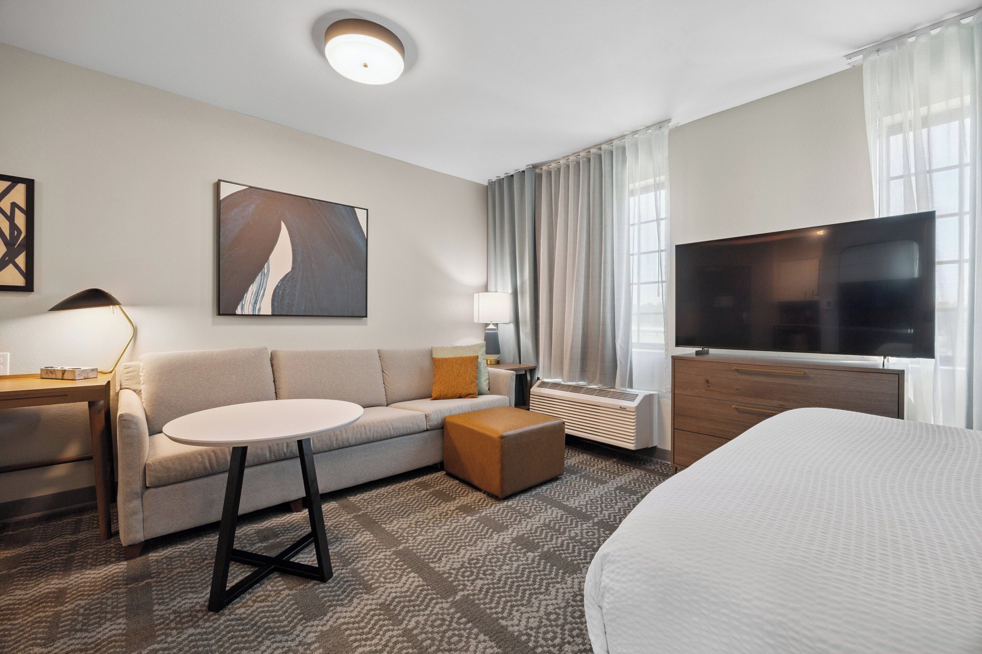 A modern hotel room with a sofa, a round table, a television, and a bed.