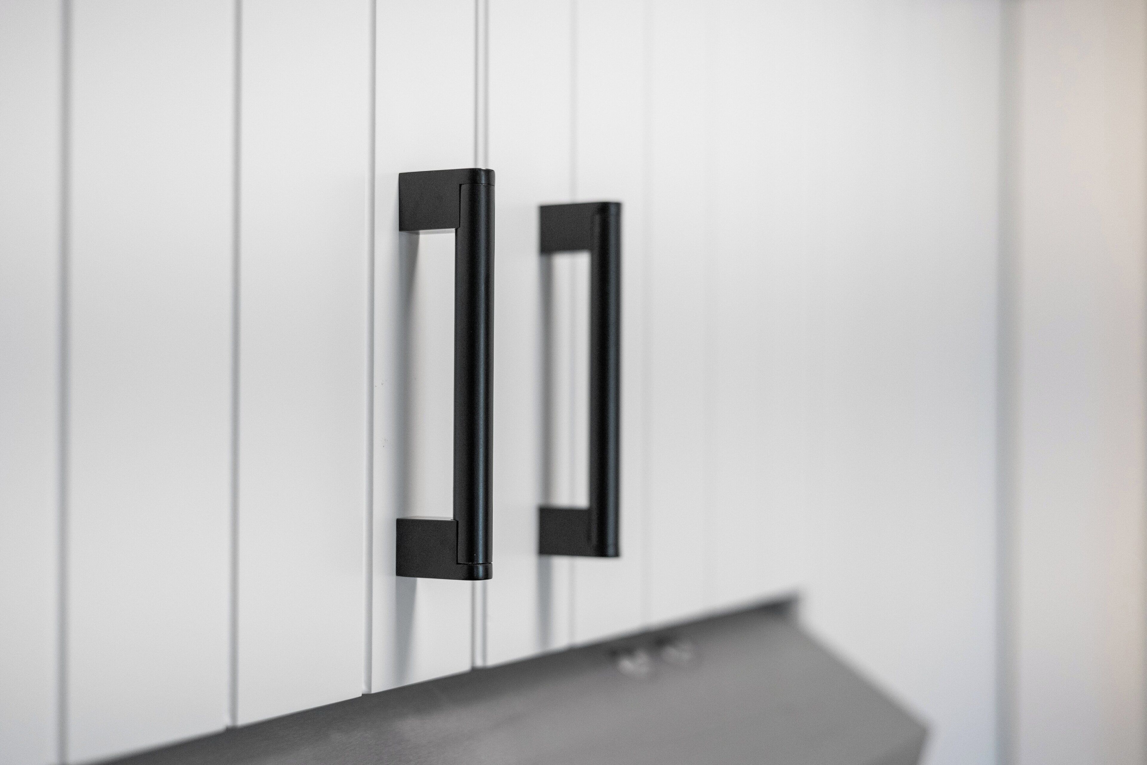 A close-up of a black handle on a white cabinet.