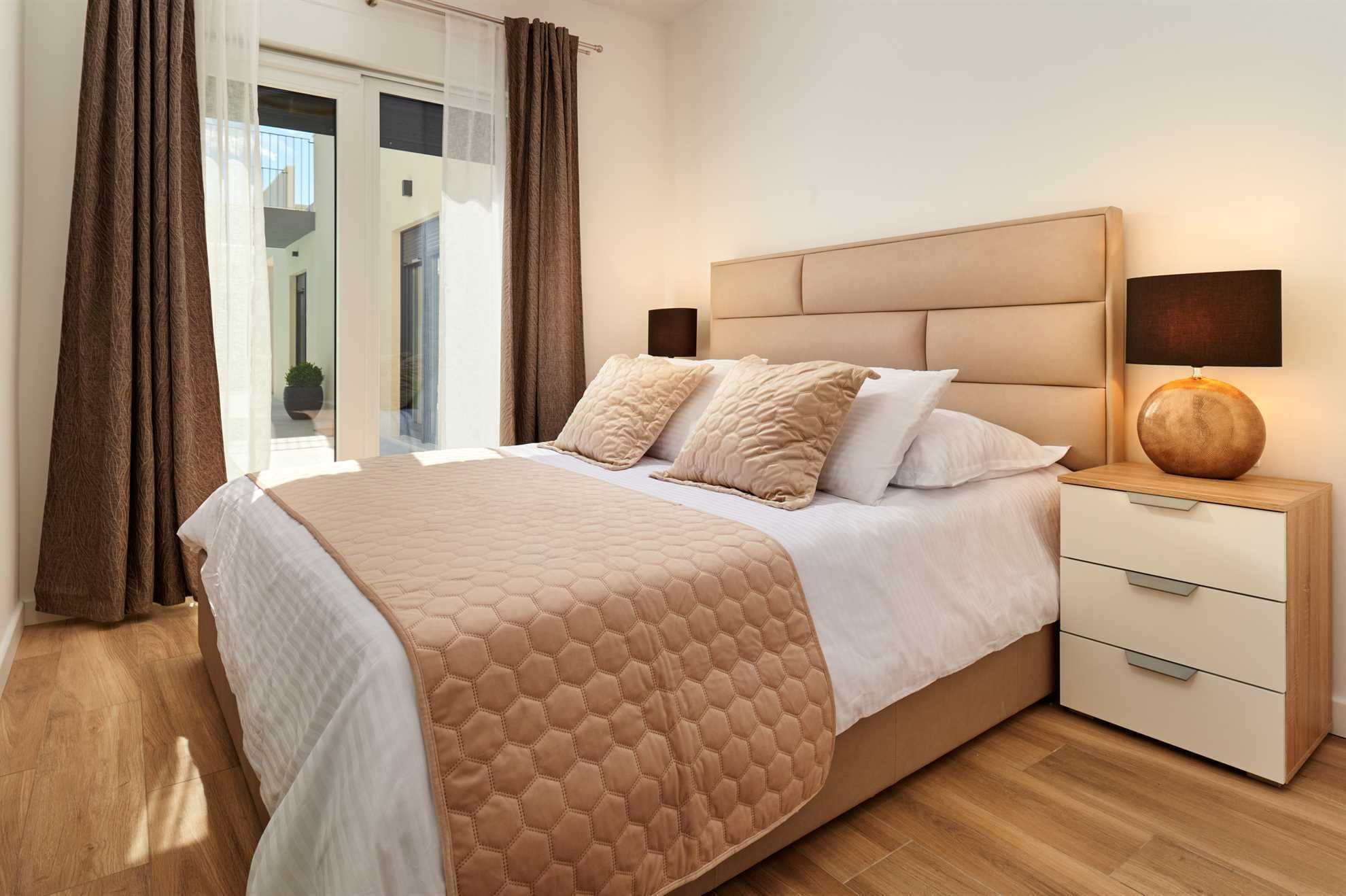 Un dormitorio con una cama grande, una mesita de noche, una lámpara y vistas al exterior.