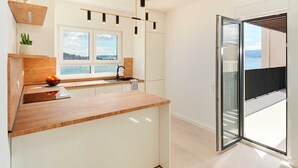 Een moderne keuken met een houten aanrecht, witte kastjes en uitzicht op zee door een groot raam.