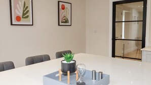 A modern meeting room with a white table, grey chairs, a potted plant, an hourglass, and two metallic containers. - Cheshire View (Buxton)