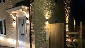 A stone building with a white door, a wooden gate, and a well-lit entrance. - Cheshire View (Buxton)
