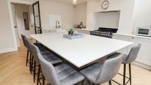 A modern kitchen with a large island, bar stools, a stove, and a microwave. - Cheshire View (Buxton)
