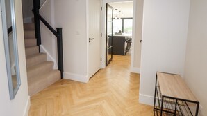 A hallway with a wooden floor, a staircase with black railings, and a door leading to a kitchen area. - Cheshire View (Buxton)