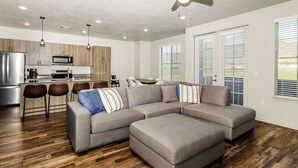 A modern kitchen with a microwave, stove, and bar stools. There is a gray sectional sofa with striped pillows and a ceiling fan. - Loaded Logan Loft near USU & EVERYTHING Else - Sleeps 8 in beds (North Logan)