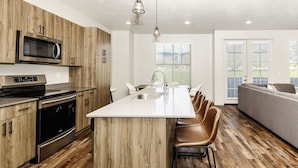 A modern kitchen with wooden cabinets, stainless steel appliances, and a central island with bar stools. - Loaded Logan Loft near USU & EVERYTHING Else - Sleeps 8 in beds (North Logan)