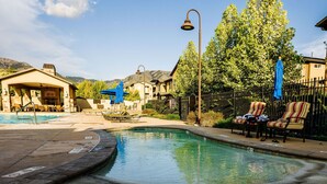 A swimming pool with lounge chairs and umbrellas, surrounded by a fence and trees. - Loaded Logan Loft near USU & EVERYTHING Else - Sleeps 8 in beds (North Logan)