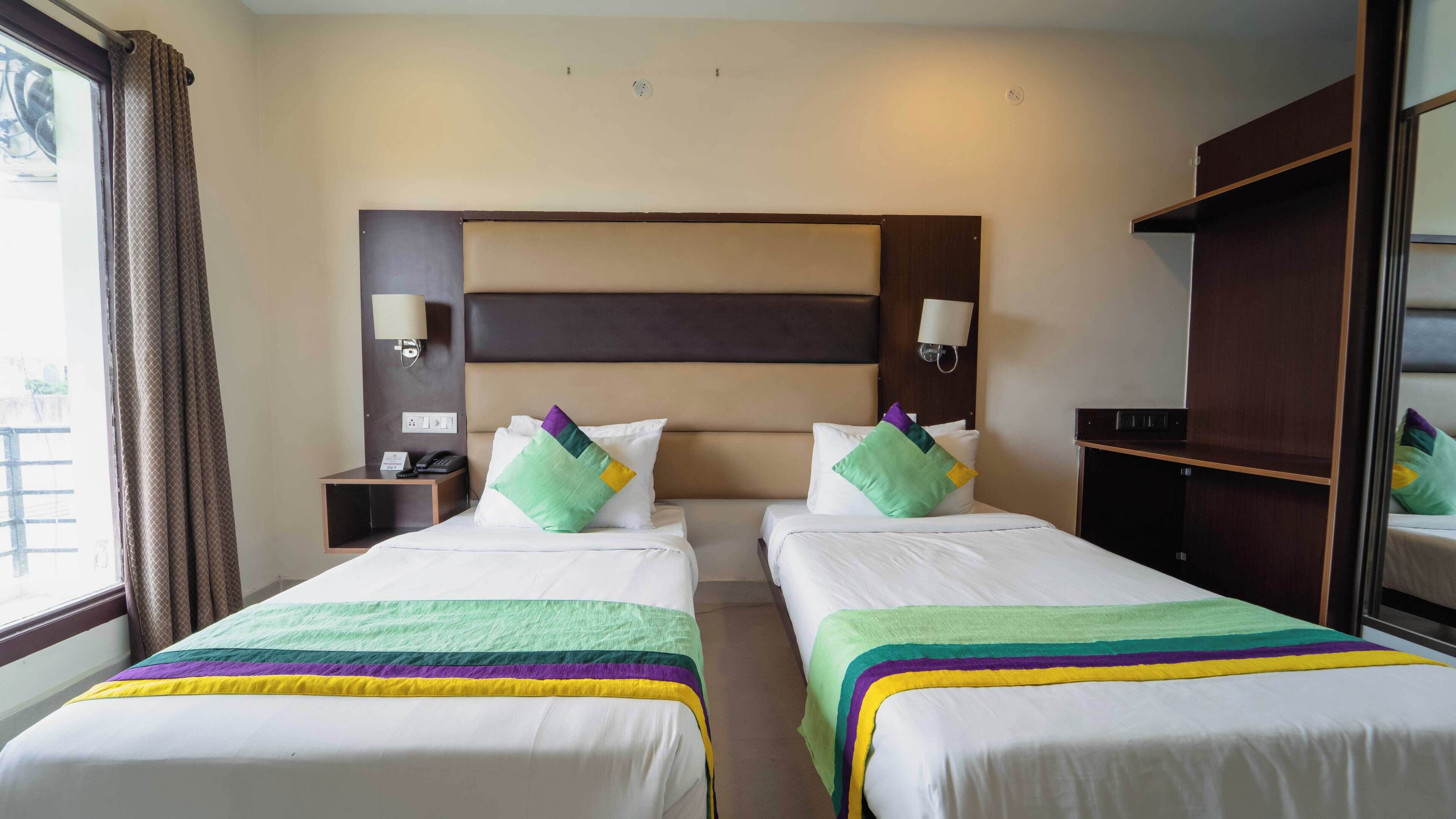 A hotel room with two beds, a headboard, bedside lamps, a nightstand, and a wardrobe.