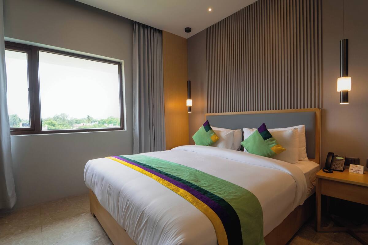 A hotel room with a large bed, a bedside table with a phone, and a window with curtains.