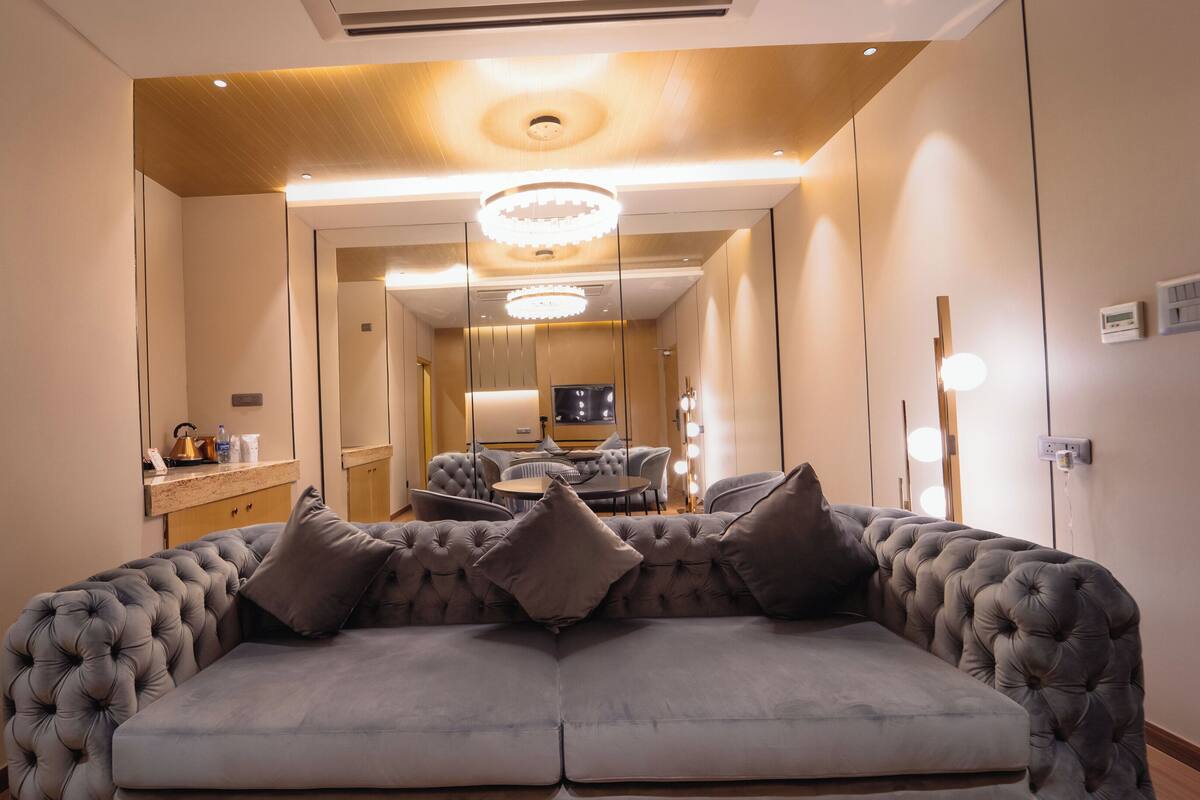 A modern hotel room with a plush sofa, a vanity with a mirror, and a chandelier.