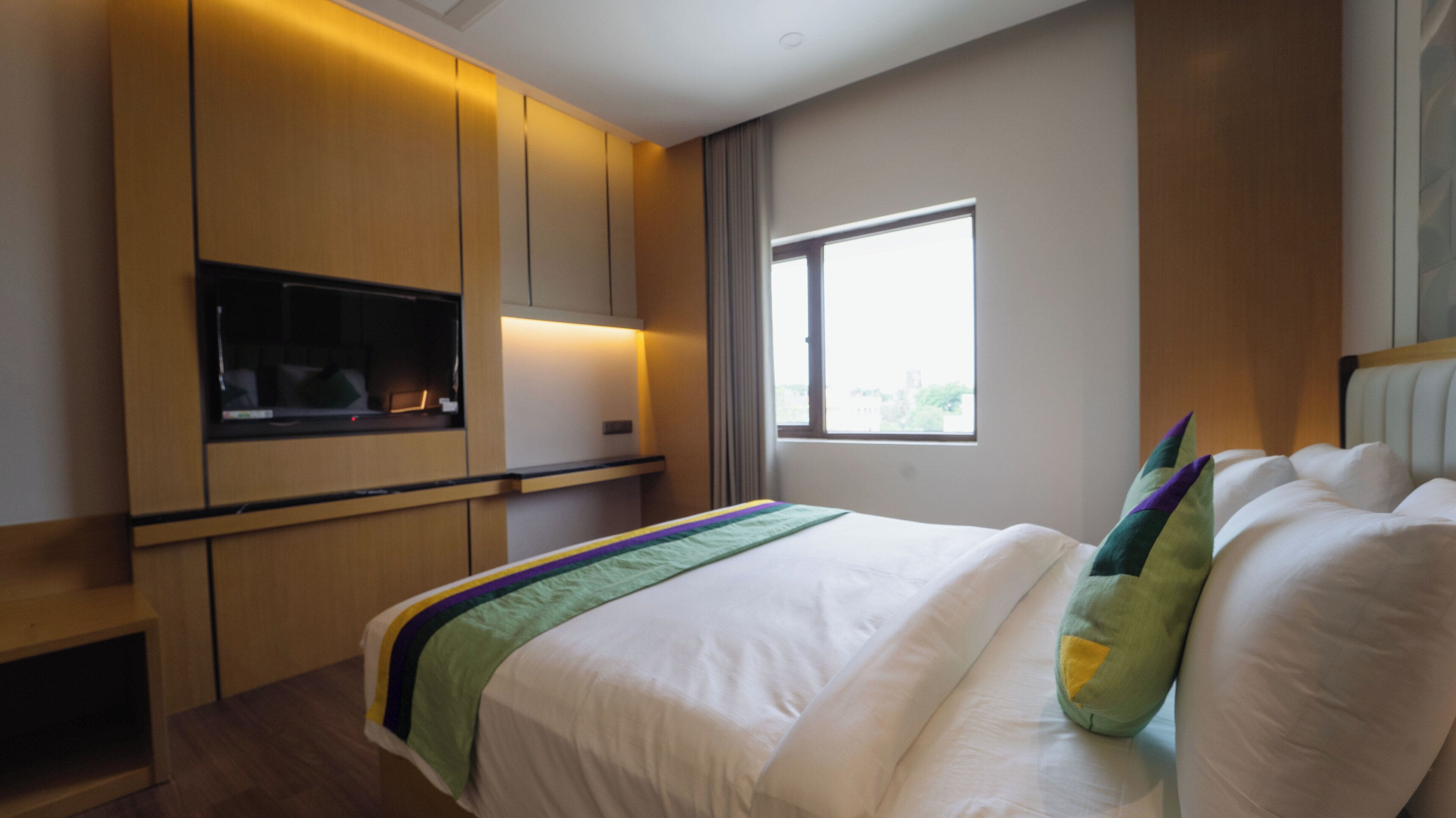 A hotel room with a bed, a TV mounted on the wall, and a window.