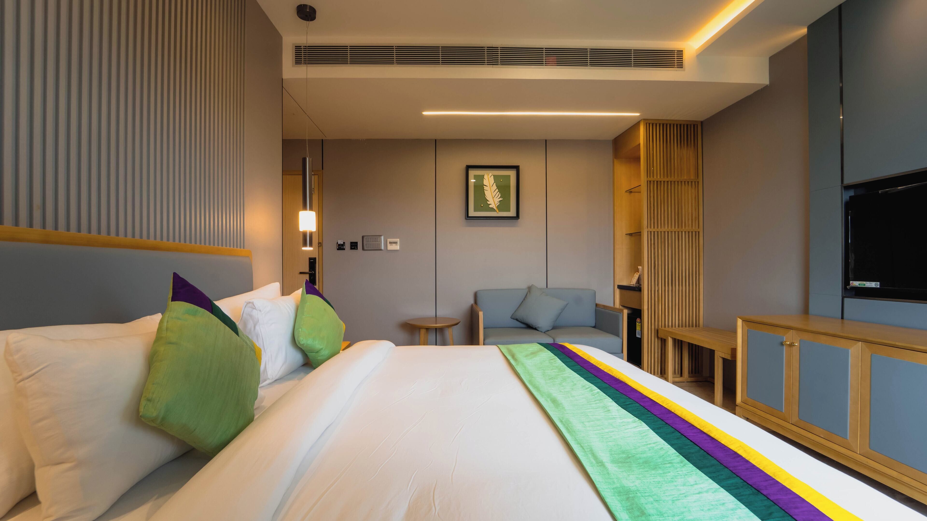 A modern hotel room with a large bed, a small sofa, a TV, and a wooden cabinet.