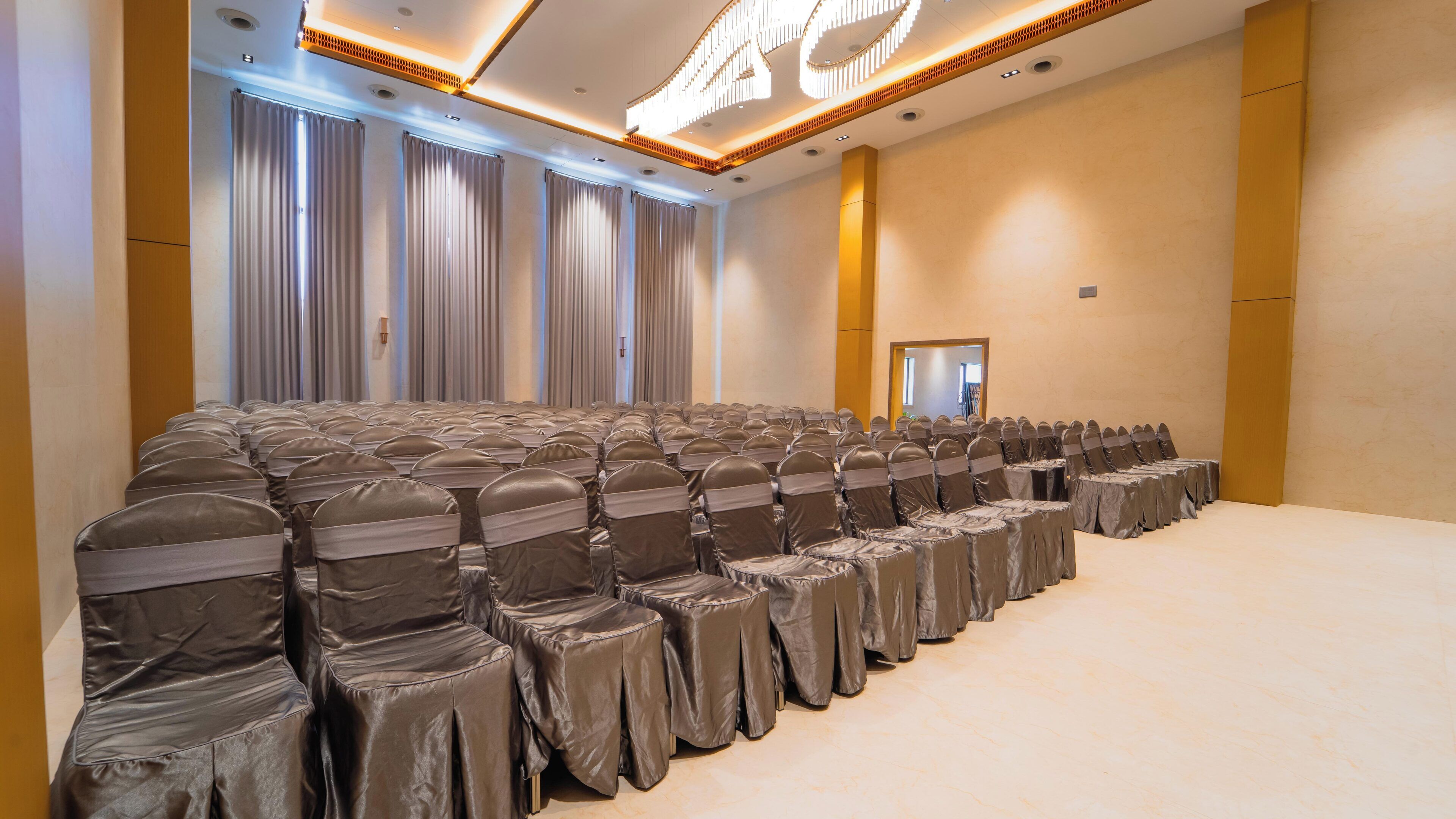 A conference room with rows of chairs and tables, a large mirror, and a ceiling with recessed lighting.