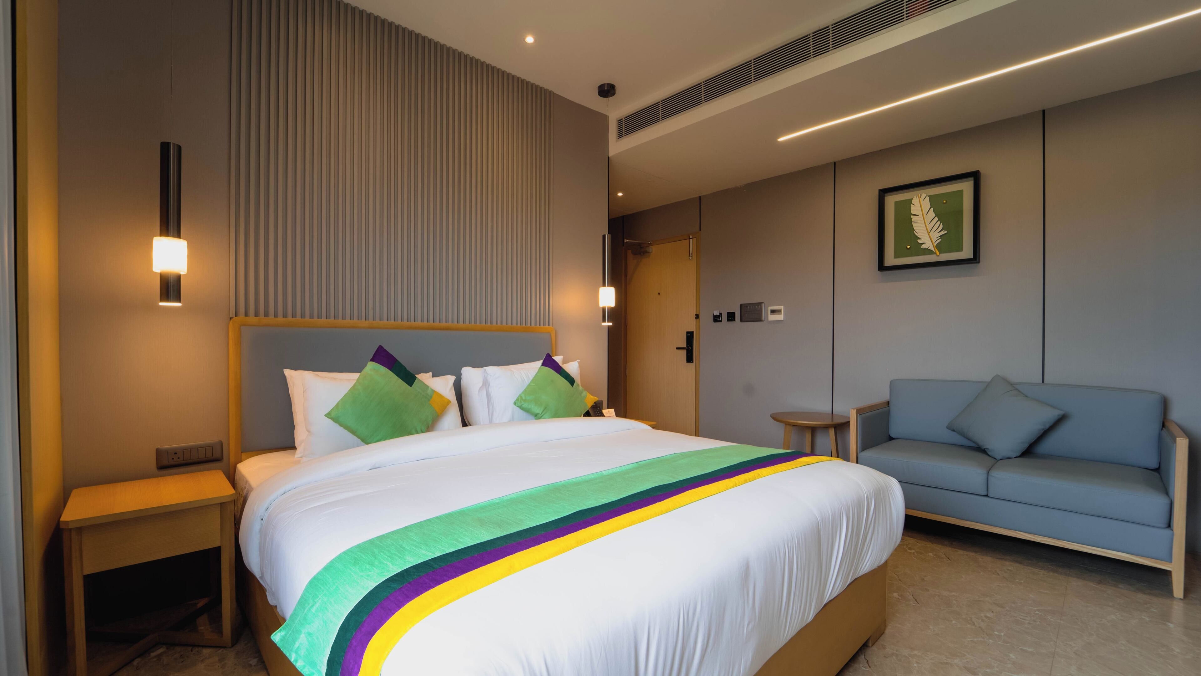 A modern hotel room with a large bed, a blue sofa, and a wall-mounted picture.
