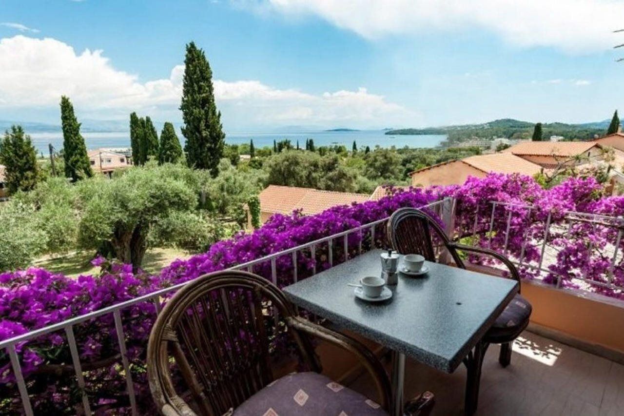Een balkon met een tafel en stoelen, met uitzicht op een schilderachtig landschap met bomen en een waterlichaam.