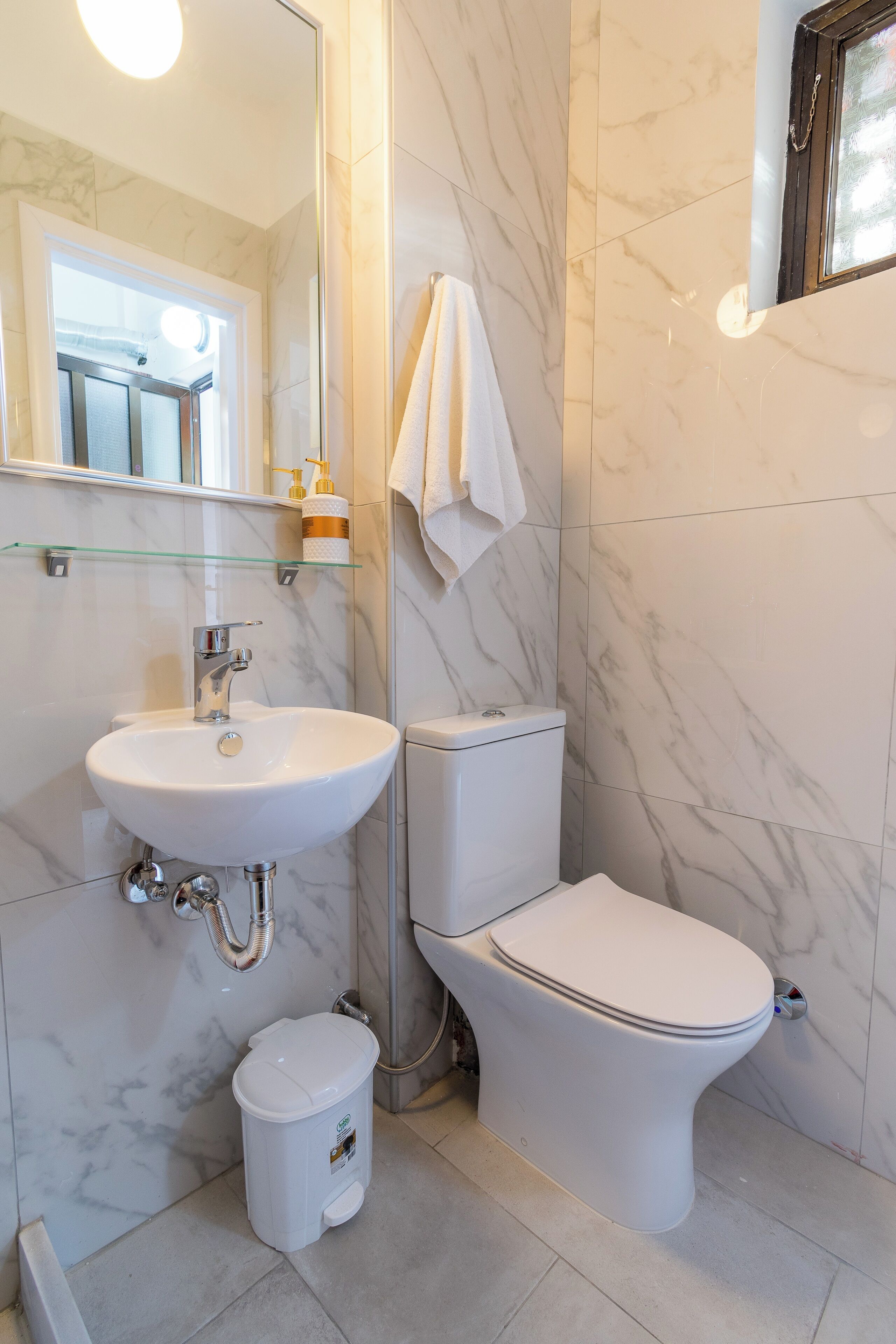 A bathroom with a white sink, toilet, and glass shelf.