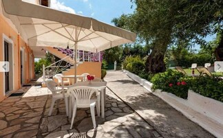 Un patio al aire libre con piso de piedra, sillas de plástico blanco, una mesa y un paraguas grande.