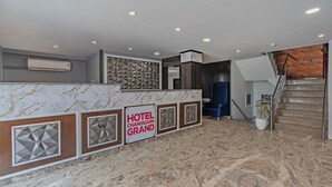 Un hall d’accueil d’hôtel avec un comptoir en marbre, une enseigne indiquant « HÔTEL CHANDIGARH GRAND » et un escalier menant à l’étage supérieur.