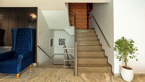 Un escalier avec une rampe métallique, un fauteuil recouvert de tissu bleu et une plante en pot.