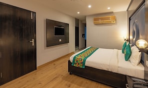 A bedroom with a bed, a TV mounted on the wall, a wooden floor, and a door. - Treebo Chandigarh Grand (Chandigarh)
