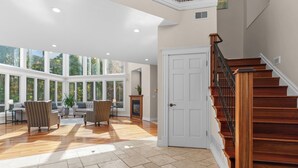 Un salon spacieux avec un escalier en bois, de grandes fenêtres et une cheminée.