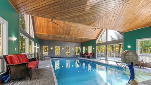 Une piscine intérieure dotée d’un plafond en bois, de murs en pierre et de sièges rouges.