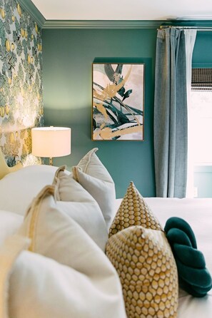 A neatly made bed with white and patterned pillows, a wall with a floral wallpaper pattern, and a framed abstract painting on the wall. - Lucky Number 7 by Pettigrew Adventures (Memphis)