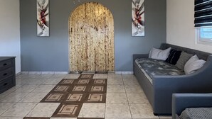 A modern living room with a ceiling fan, a grey sofa, a patterned rug, and a wooden wall panel. - Villa Destiny Family Friendly Destination with private pool & jacuzzi &more. (Cacao)