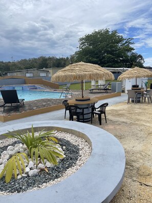 Un área de piscina con sillas de descanso, una zona de barbacoa y sombrillas de paja.