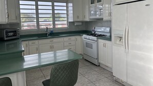 A kitchen with white cabinets, a stove, a refrigerator, a window with blinds, and a green countertop. - Villa Destiny Family Friendly Destination with private pool & jacuzzi &more. (Cacao)