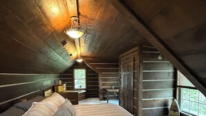 Un dormitorio acogedor en el ático, con una cama grande, paredes de madera, un ventanal pequeño y un techo inclinado.