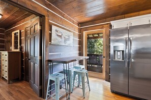 Interior de madera con zona de cocina, que incluye un refrigerador, taburetes de bar y un armario de madera.