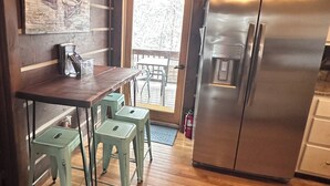 Una cocina con una mesa de madera y taburetes, un refrigerador de acero inoxidable y una puerta que da a un área exterior.