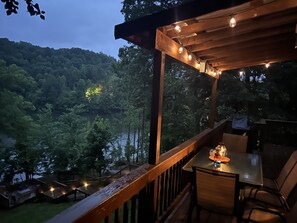 A wooden deck with a table and chairs, overlooking a forested area and a body of water.