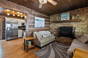 Una sala de estar moderna con chimenea de piedra, una cocina con electrodomésticos de acero inoxidable y techo de madera.