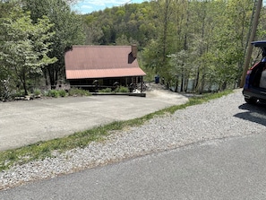 A building with a red roof and a covered area with a concrete floor, surrounded by trees and a gravel path.
