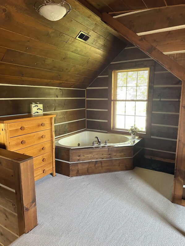 A cabin bathroom with a wooden vanity, a freestanding bathtub, and a window with blinds.