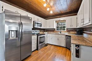 Una cocina moderna con electrodomésticos de acero inoxidable, piso de madera y muebles de color blanco.