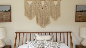 A bedroom with a bed, wooden headboard, two bedside tables, and macramé wall hangings. - Chic Catskills Cabin w/ Fireplace, Firepit, 30min to Ski Big Bear Resort. (Cochecton)