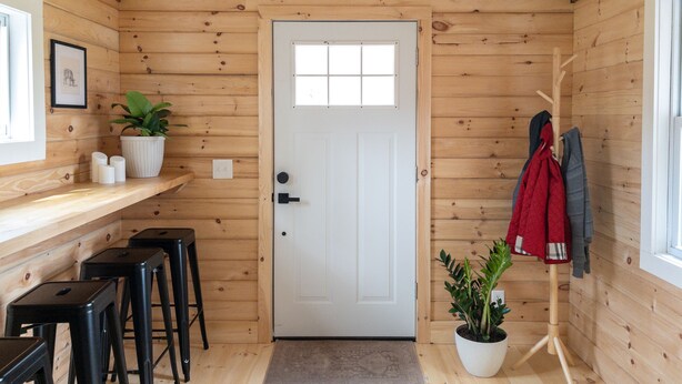 A wooden interior with a white door, a hanging light fixture, a potted plant, and a coat rack with jackets. - Chic Catskills Cabin w/ Fireplace, Firepit, 30min to Ski Big Bear Resort. (Cochecton)