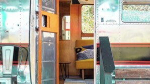 A vintage camper van interior with a wooden bench, a small table, and a window with a view of greenery. - Stunning View. Romantic Airstream, Sauna, Fire Table, Hot Tub, Cold Plunge (Weaverville)