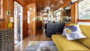 A cozy interior with a wooden floor, a sofa with patterned cushions, a dining area, and a kitchen visible through the windows. - Stunning View. Romantic Airstream, Sauna, Fire Table, Hot Tub, Cold Plunge (Weaverville)