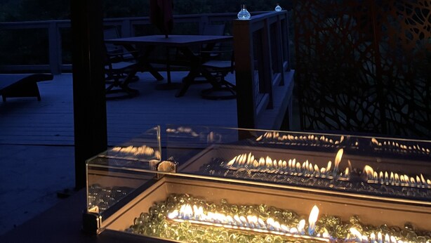 A dimly lit outdoor patio with a table and chairs, overlooking a mountainous landscape. - Stunning View. Romantic Airstream, Sauna, Fire Table, Hot Tub, Cold Plunge (Weaverville)