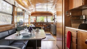 A compact dining area with a table, chairs, and a bench. A kitchenette with a stove and cabinets is visible. - Stunning View. Romantic Airstream, Sauna, Fire Table, Hot Tub, Cold Plunge (Weaverville)