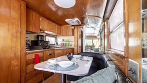 A compact kitchen with wooden cabinets, a stove, and a dining table with a few chairs. - Stunning View. Romantic Airstream, Sauna, Fire Table, Hot Tub, Cold Plunge (Weaverville)