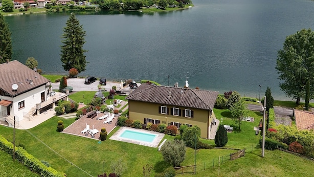 En fastighet vid sjön med en swimmingpool, en tennisbana och utsikt över sjön och bergen.